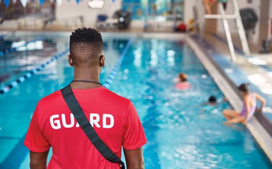 a photo of the back of a lifeguard looking at a pool with swimmers 