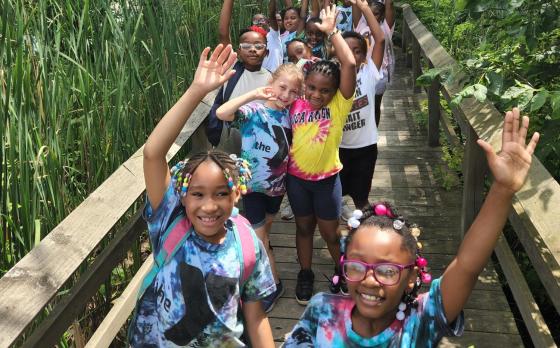 A group of kids from power scholars walking on a wooden walking bridge outside