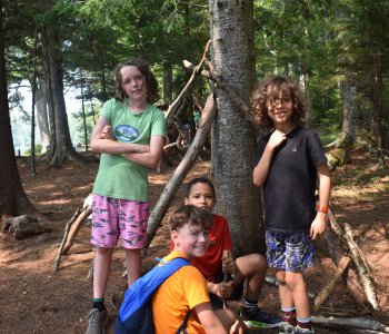 a group of boy campers smile by a tree as they explore the wilderness