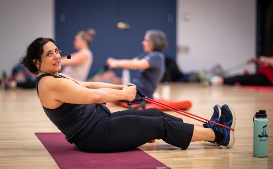 Group Exercise instructor sitting down with exercise bands looped around their feet for a workout