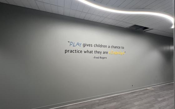 artwork on the wall in the Mickey Sands Child Care Center that is a quote from Fred Rogers (Mr. Rogers) that reads "Play gives children a chance to practice what they are learning."