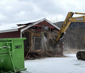 excavator being operated by BOCES student removing the outside wall of a cabin on property at The Y at Watson Woods