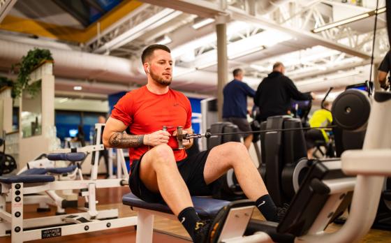 Man in orange shirt and black shorts working out on a row machine
