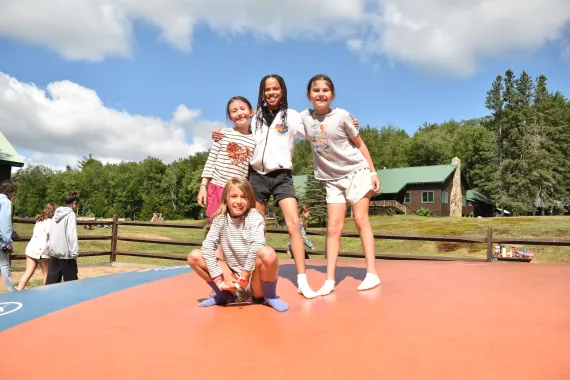 a group of girl campers smile on the bounce pillow, hugging