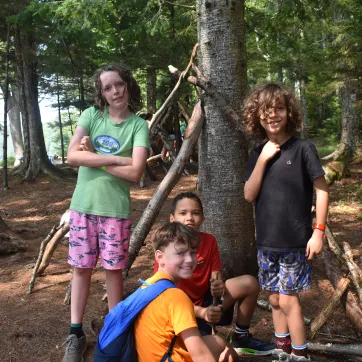 a group of boy campers smile by a tree as they explore the wilderness
