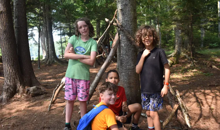 a group of boy campers smile by a tree as they explore the wilderness