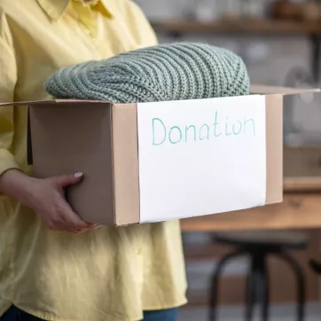 a woman holding a cardboard box labeled donation with a blanket sticking out from the box