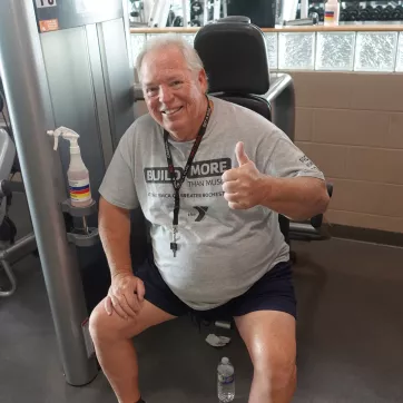an older man sitting on a strength machine smiling and giving a thumbs up