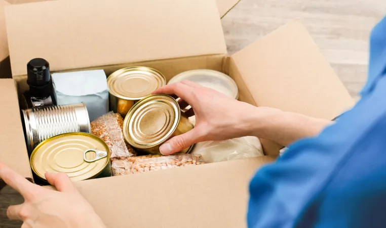 photo of person fill cardboard box with nonperishable foods and canned goods 