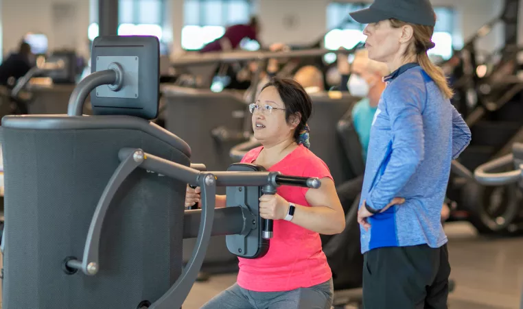 ymca member works out on egym equipment while staff helps give tips