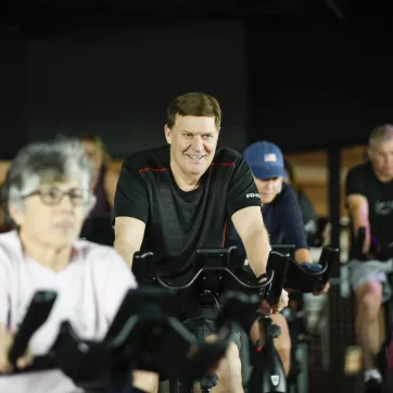 Man smiles while cycling in a YMCA group exercise class