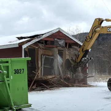 excavator being operated by BOCES student removing the outside wall of a cabin on property at The Y at Watson Woods